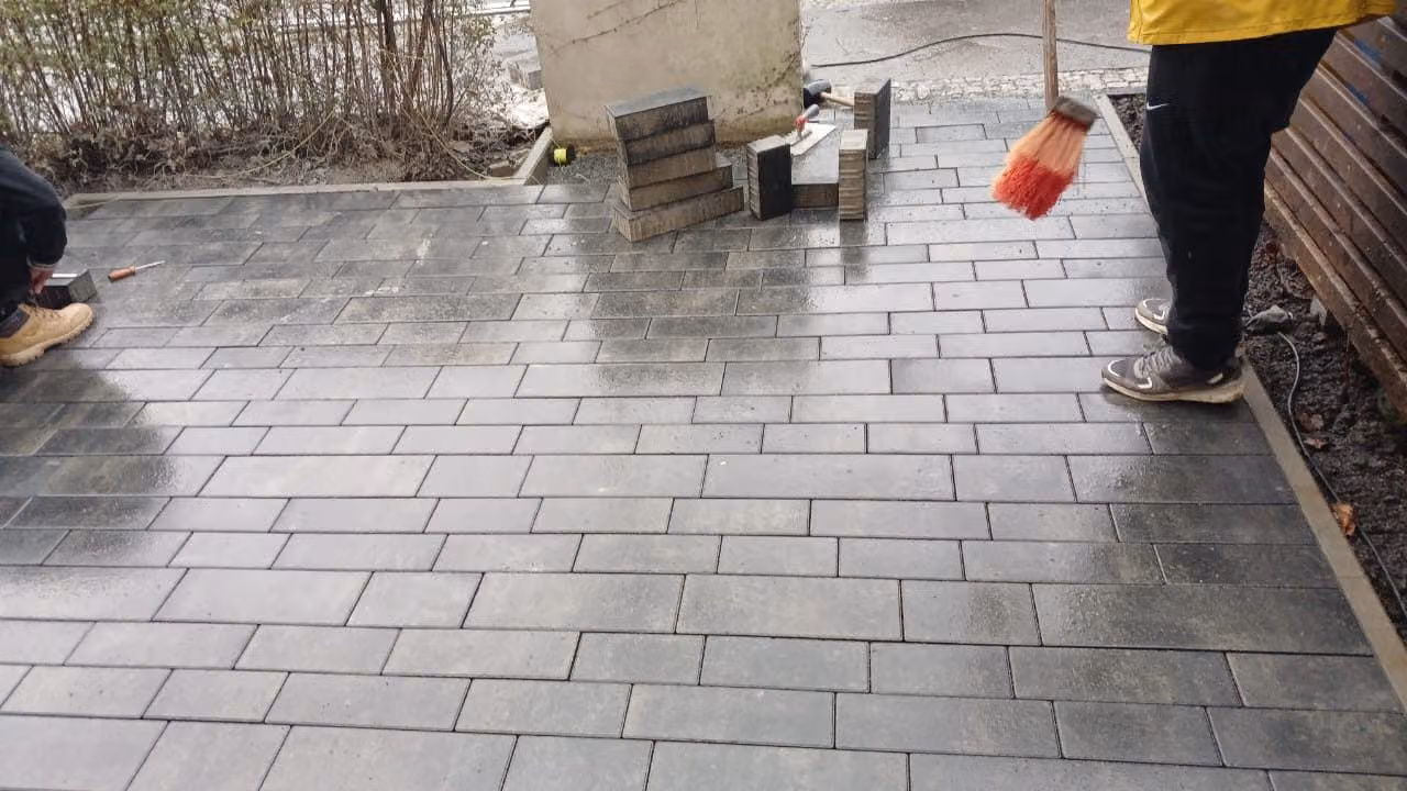 Verlegen von grauem Betonpflaster im Läuferverband bei Regen