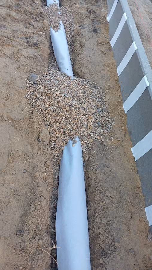 Filterkies wird auf das vliesummantelte Drainrohr am Fundament aufgebracht