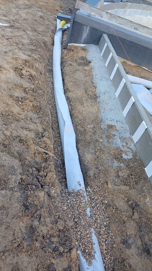 Vliesummanteltes Drainrohr im Graben am Fundament, Filterkies teilweise eingebaut