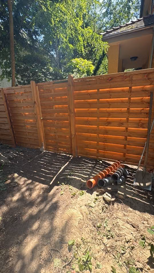 Sichtschutzzaun aus Holz mit Tor im Garten, Fläche davor vorbereitet
