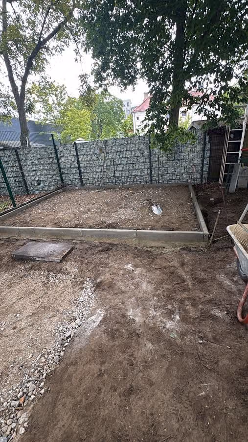 Vorbereitetes Plattenfundament für zwei Gartenschuppen, dahinter Sichtschutzzaun mit Folie