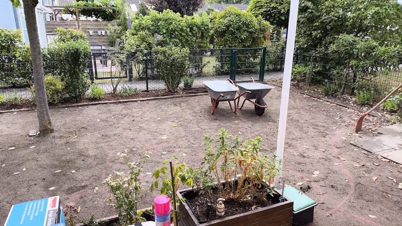 Vorbereitete Gartenfläche mit markiertem Verlauf, Schubkarren und Werkzeug bereitgestellt