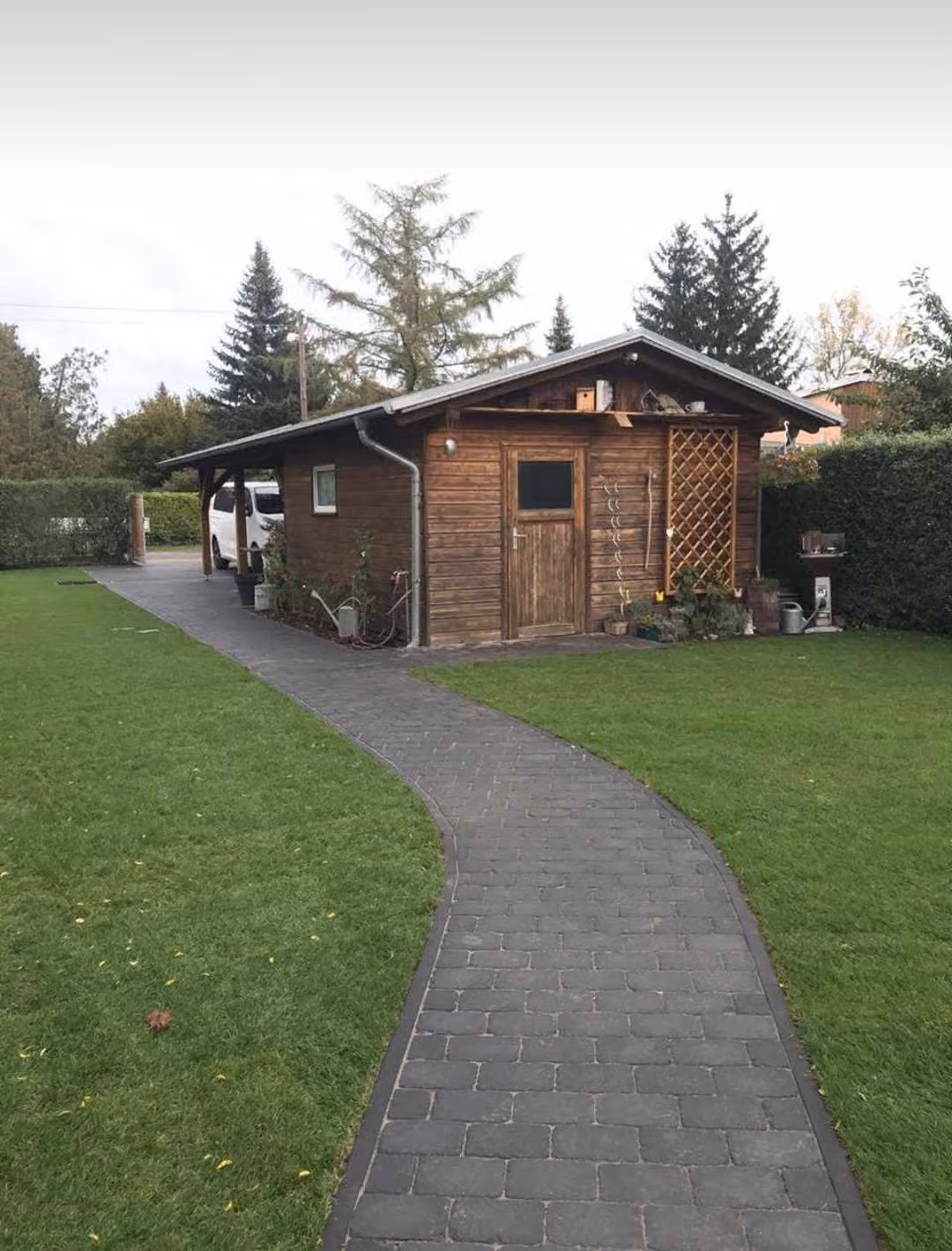 Pflasterweg mit dunkler Randzeile führt am Gartenhaus vorbei zum Carport