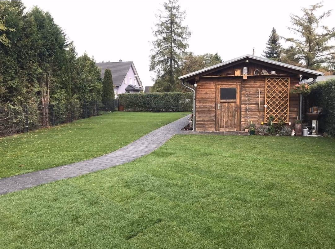 Geschwungener Pflasterweg über den Rasen zum Gartenhaus mit Carport
