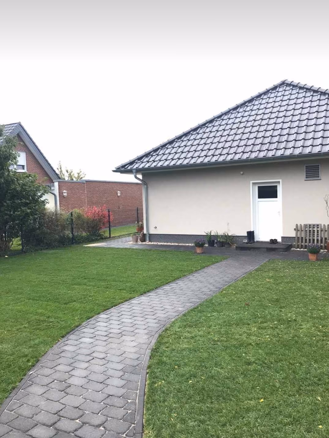 Geschwungener Pflasterweg aus Betonstein führt über den Rasen zum Hauseingang