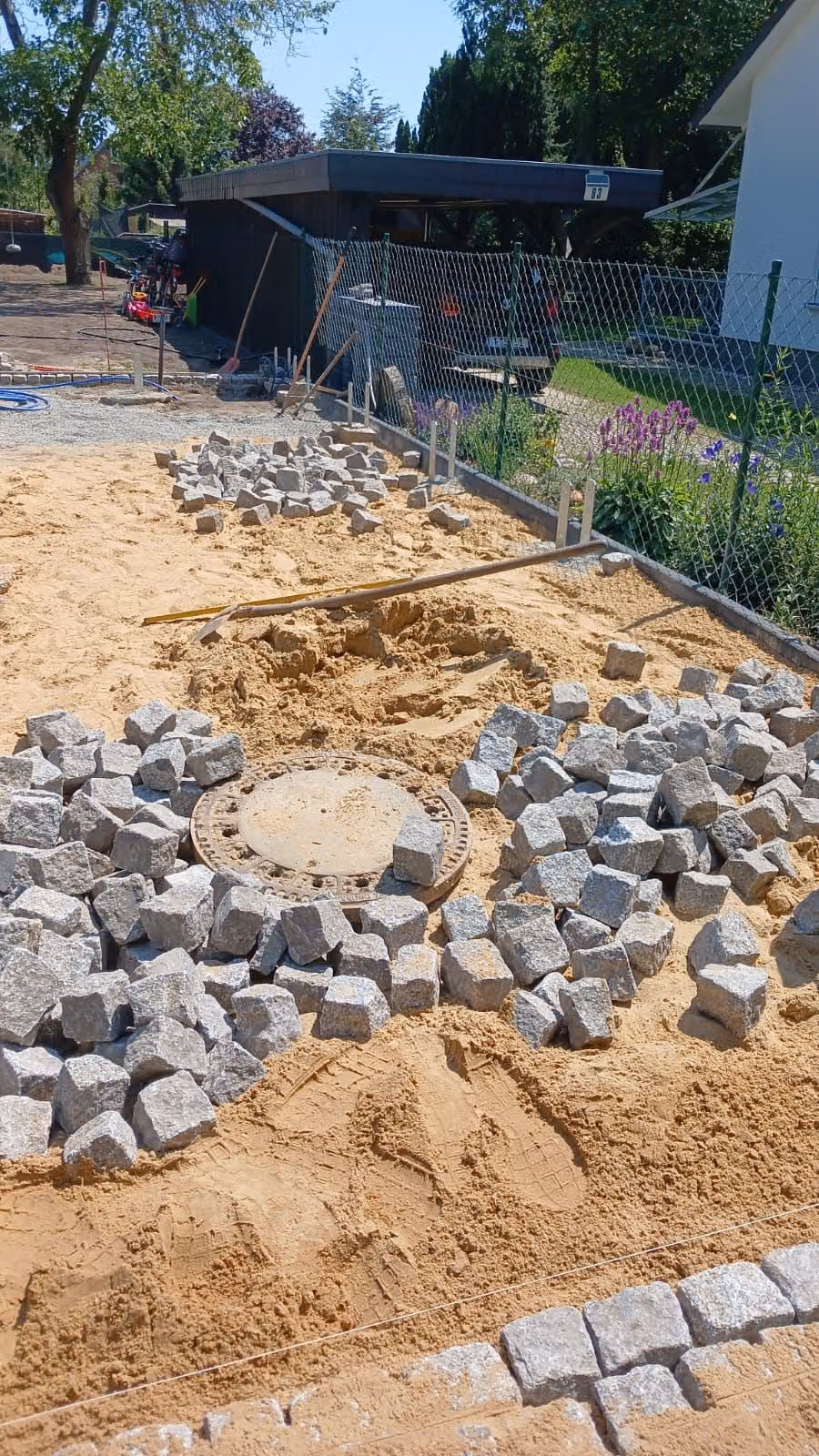 Granit-Kleinpflaster wird im Kreisverband um einen Kontrollschacht gesetzt