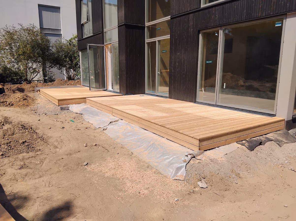 Fertige Holzterrasse aus hellen Dielen direkt an der dunklen Holzfassade