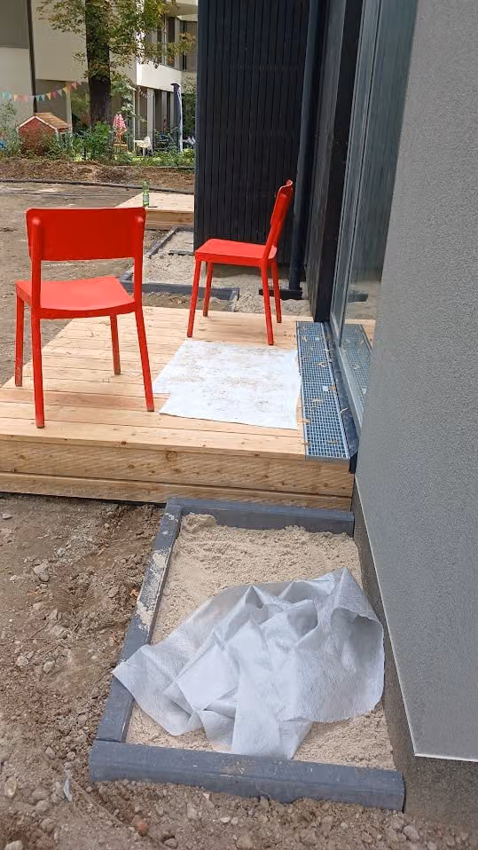 Holzterrasse mit Stühlen und umlaufendem Metall-Randprofil zum Kiesstreifen