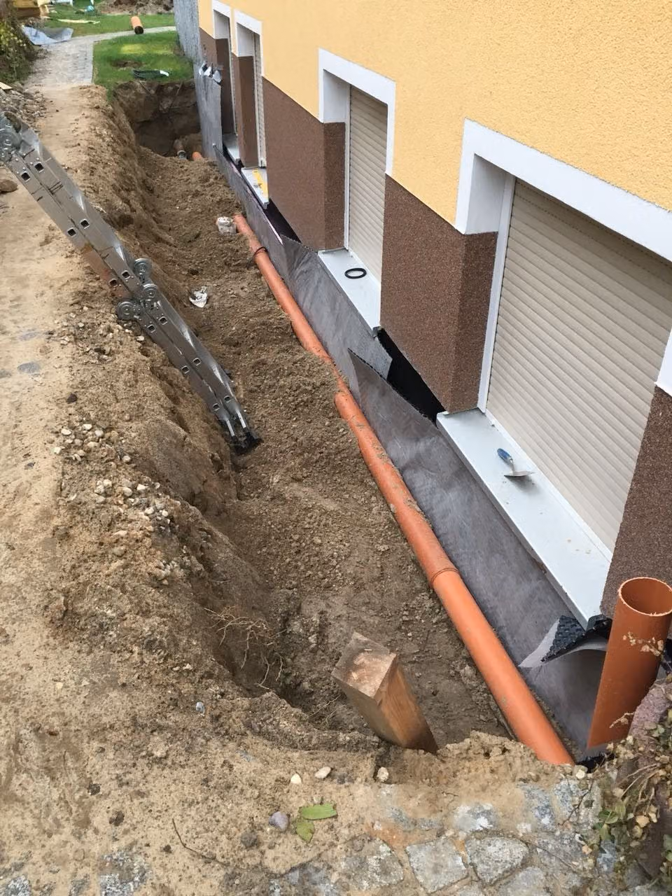 Freigelegte Kellerwand mit Abdichtung, Noppenbahn und verlegter Drainage