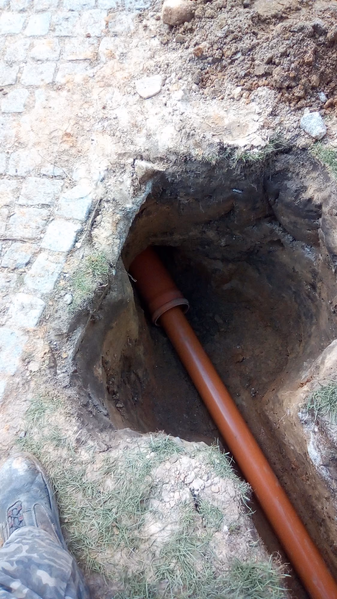 KG-Rohr-Anschluss in der Baugrube neben einem Natursteinpflasterweg