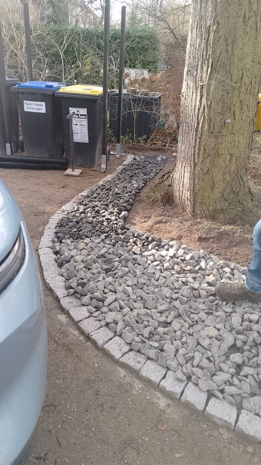 Schotterstreifen mit Kleinpflasterkante an einer Hausfassade