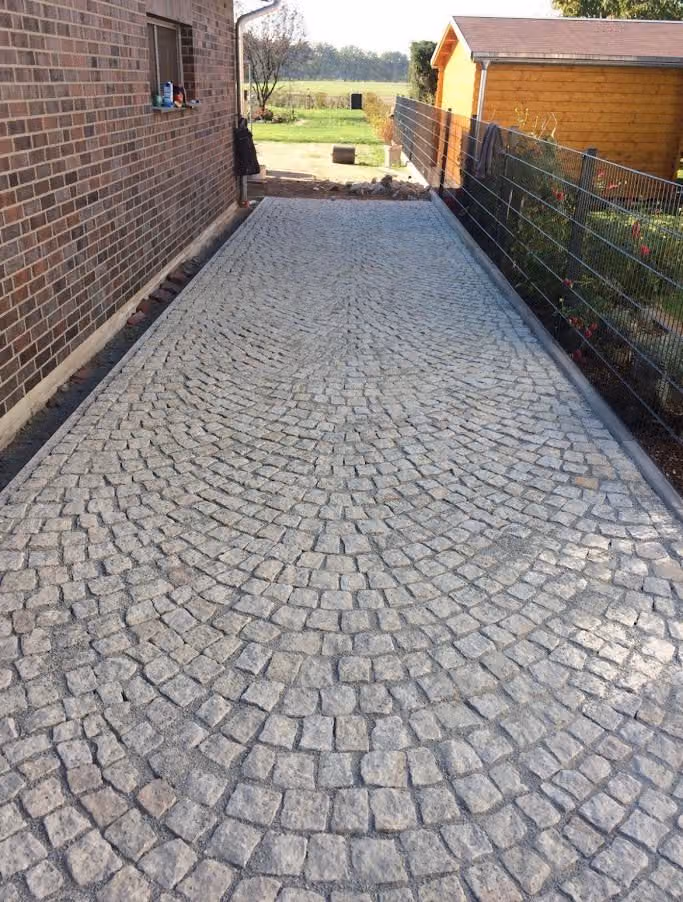 Fertige Zufahrt aus Granit-Kleinpflaster im Segmentbogenverband zwischen Haus und Zaun