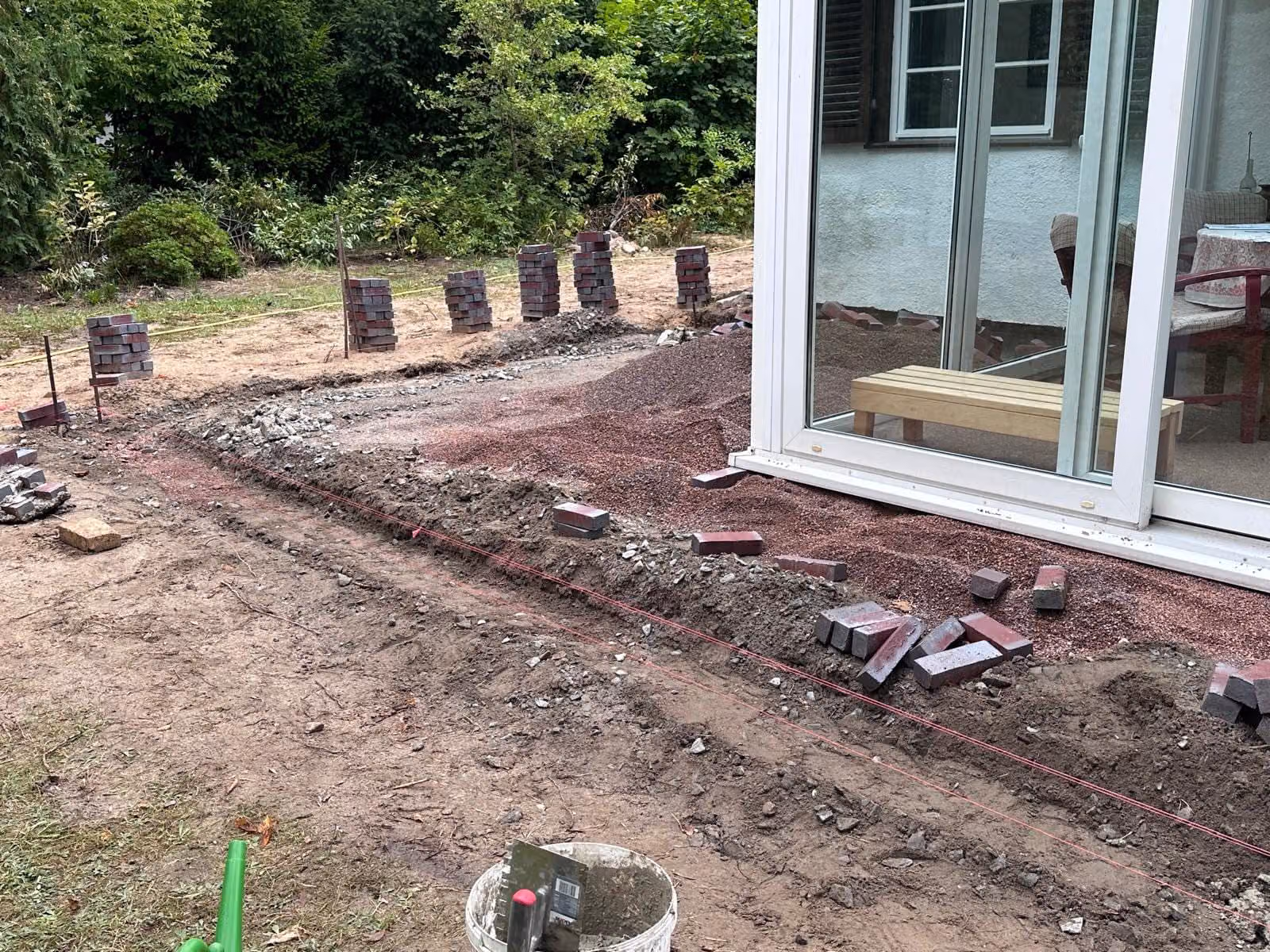 Baustelle an der Terrassentür: ausgehobener Graben, Klinker in Stapeln entlang der gespannten Schnur bereitgelegt