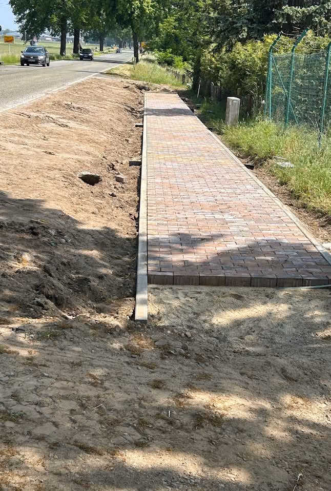 Fertiger Gehweg aus rotbraunem Pflaster im Läuferverband mit Granitbord entlang der Straße