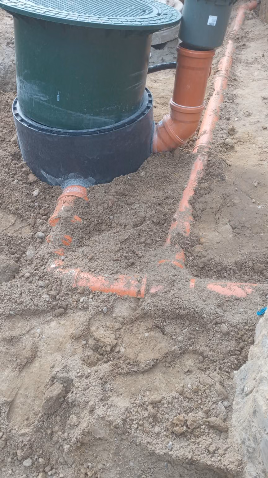 Kontrollschacht mit angeschlossenen KG-Rohren im Sandbett vor dem Verfüllen