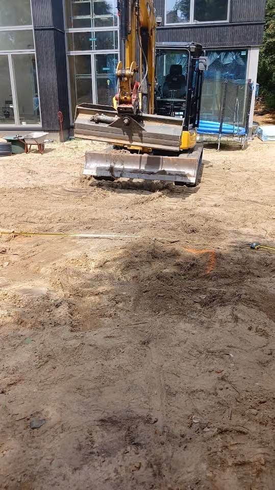 Bagger transportiert Terrassenplatten über das Sandplanum vor dem Neubau