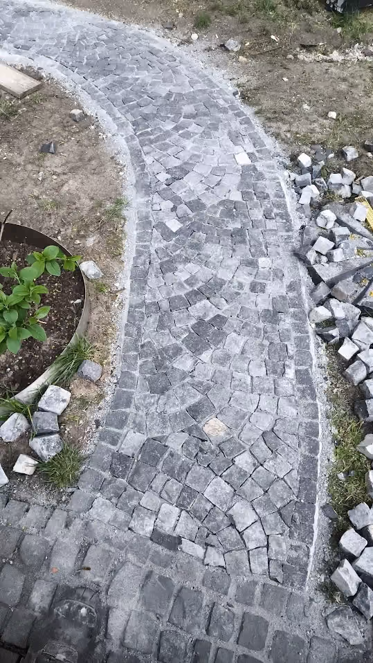Geschwungener Gartenweg aus dunklem Granit-Mosaikpflaster im Bogenverband, Restmaterial daneben