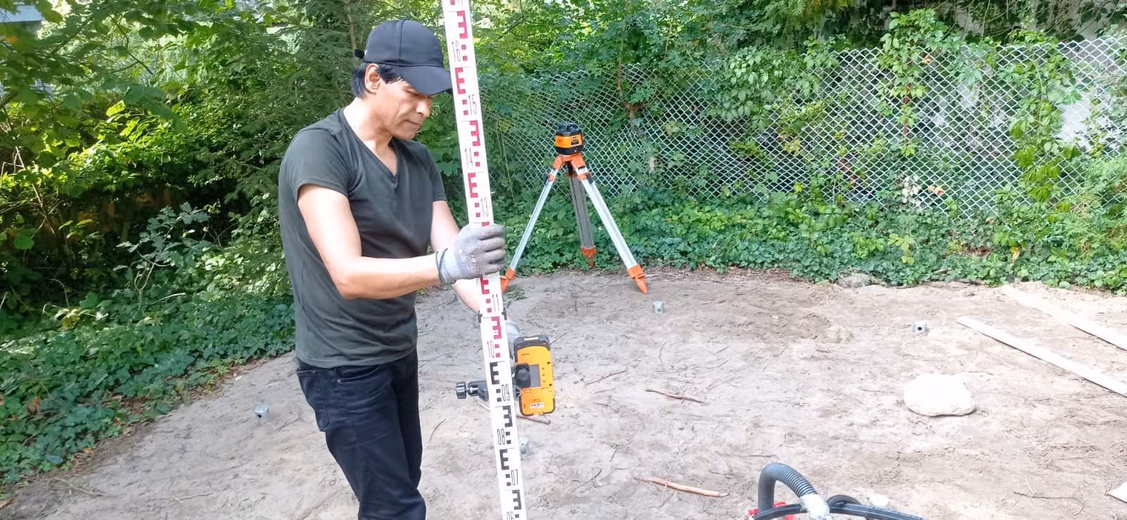 Mann hält eine Nivellierlatte mit Laserempfänger, dahinter steht der Rotationslaser auf dem Stativ