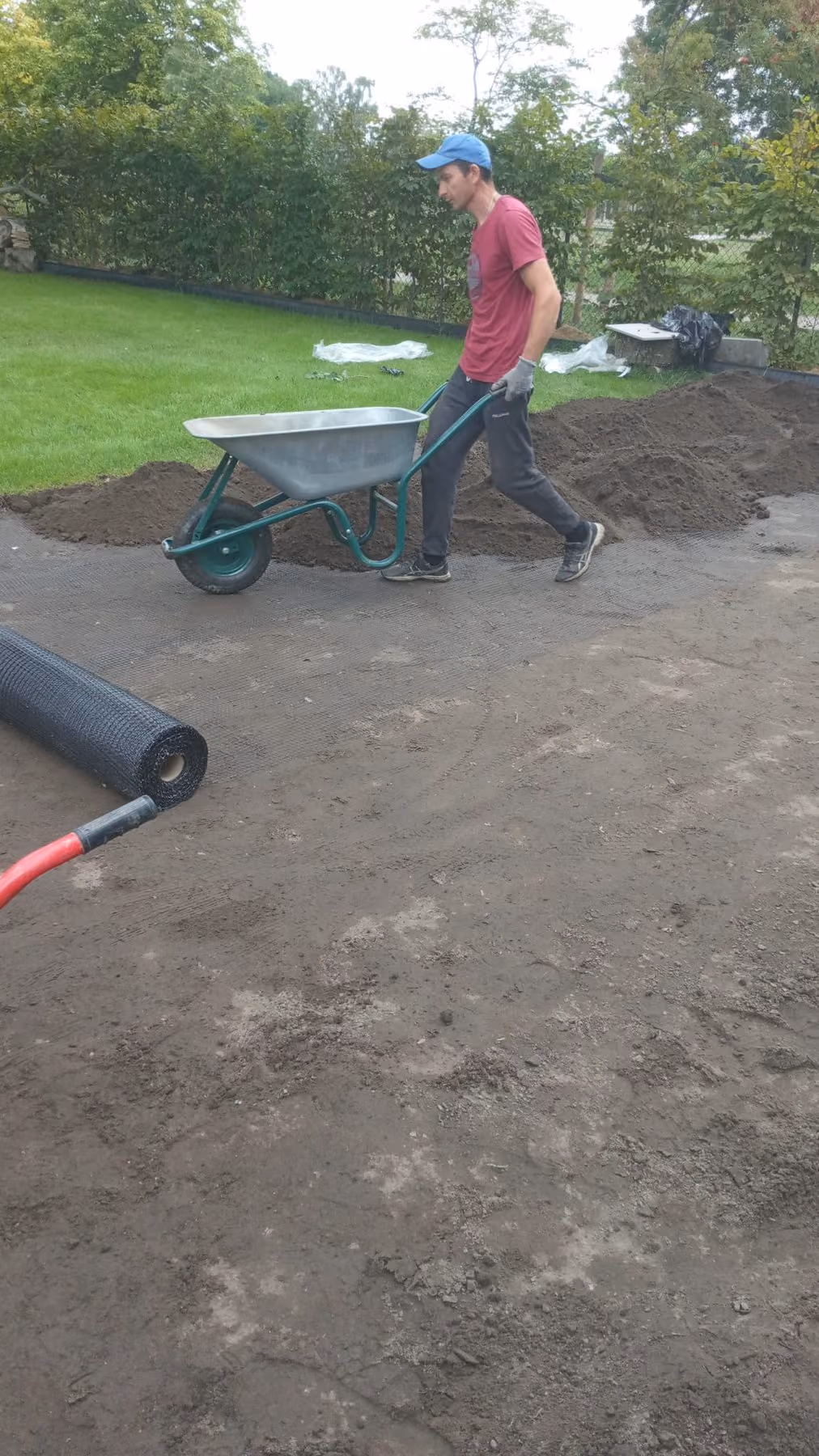 Arbeiter bringt Oberboden mit der Schubkarre auf die vorbereitete Rasenfläche