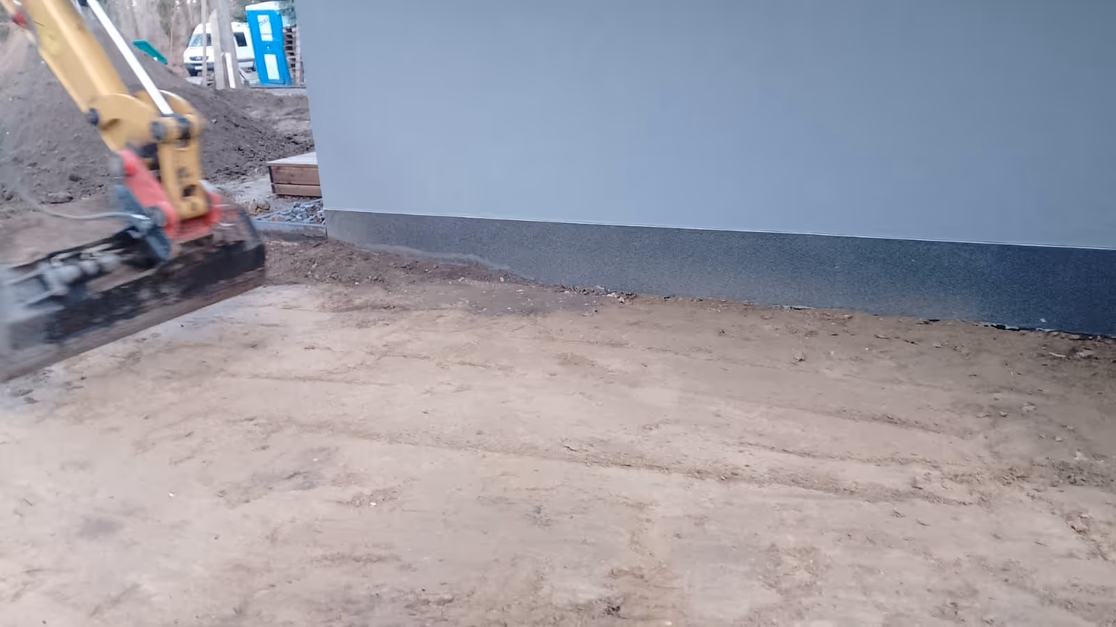 Bagger stellt das Planum entlang der Hausfassade nach dem Rohbau her