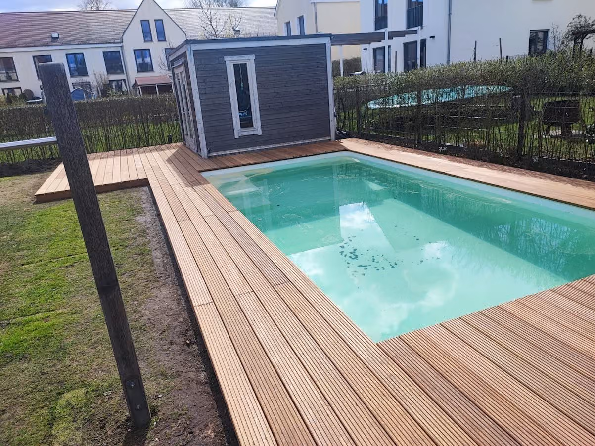 Pool mit umlaufender Holzterrasse und angrenzendem Saunahaus im Reihenhausgarten