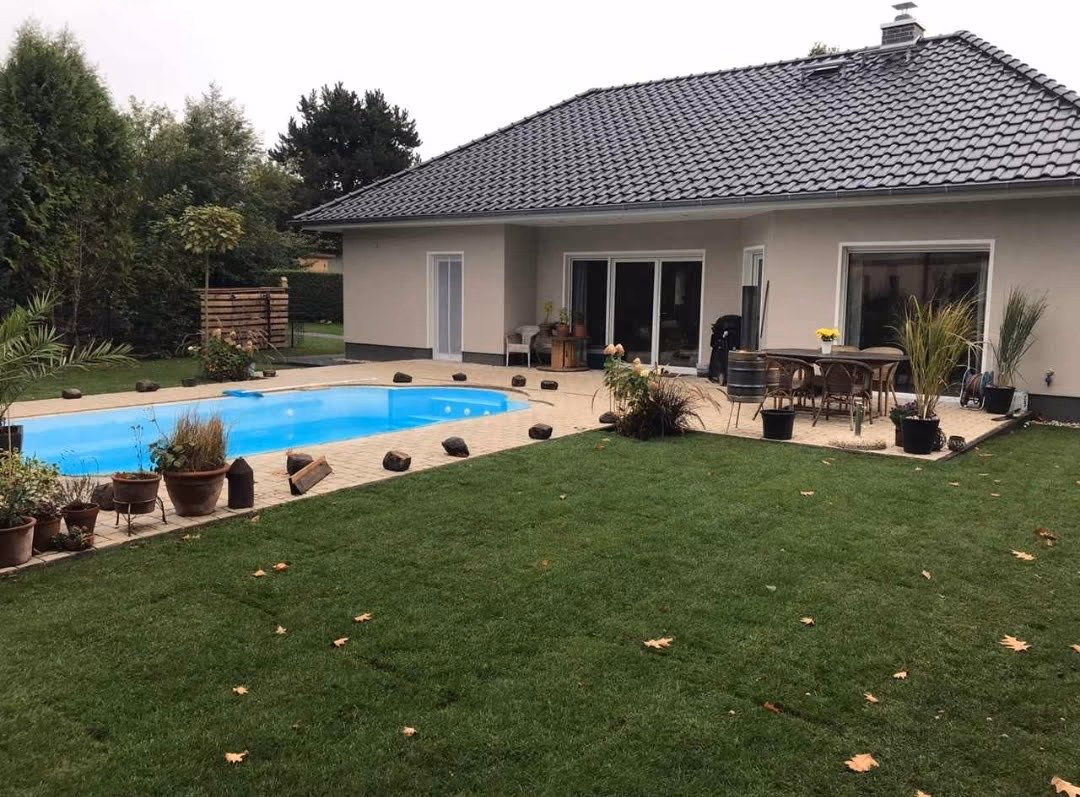 Fertige Poolterrasse mit Rasenfläche, Pflanzkübeln und Sitzplatz am Bungalow