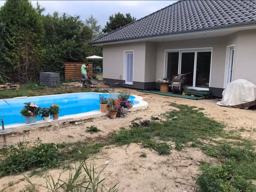 Poolbecken im Rohbau, umgeben von Sandfläche und Baumaterial