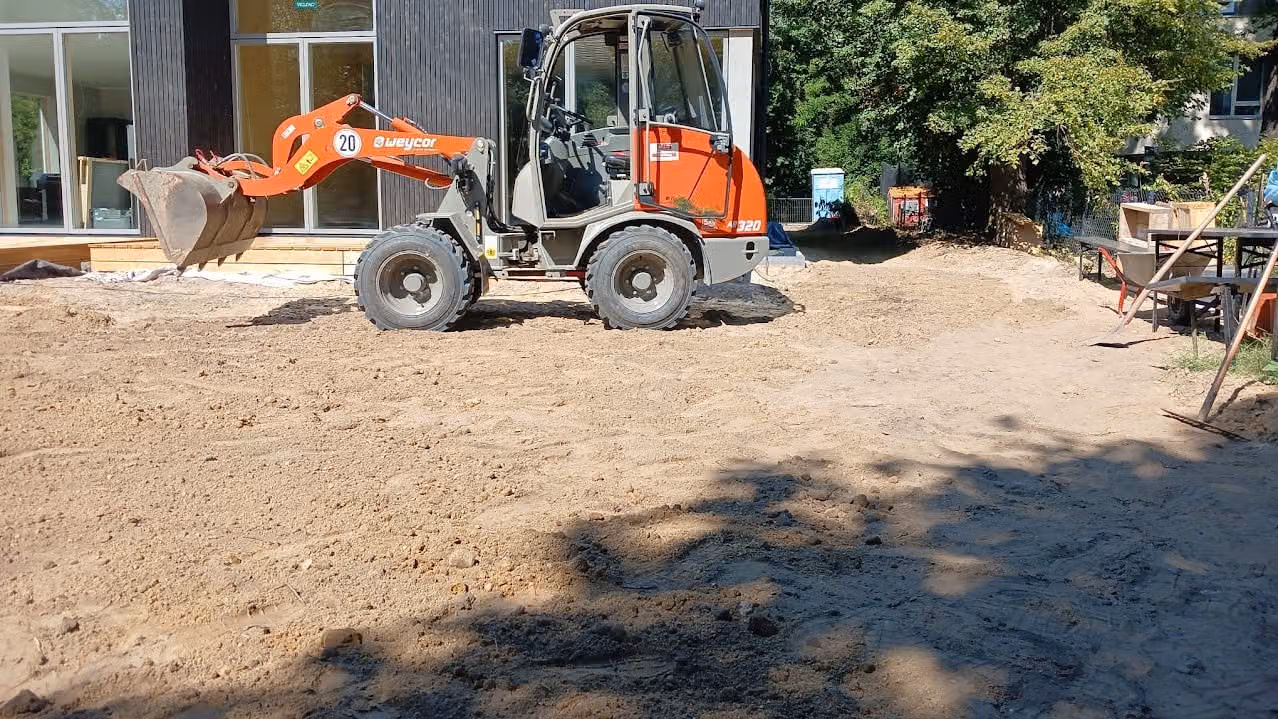 Radlader auf dem abgezogenen Sandplanum vor einem Neubau mit Holzfassade