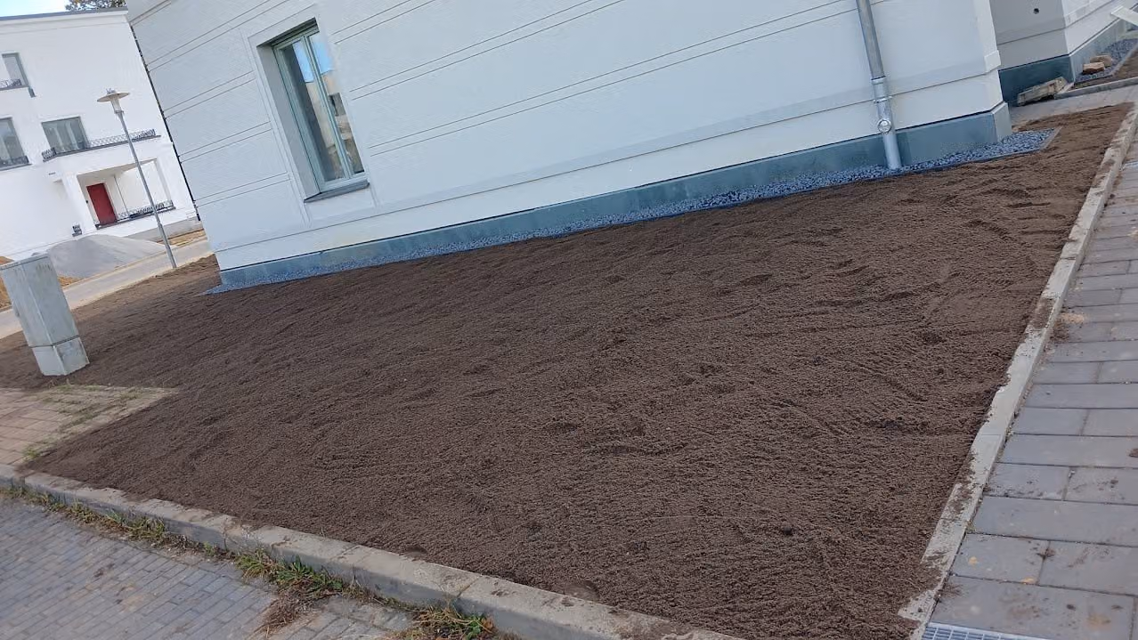 Vorbereitetes Saatbeet entlang des Pflasterwegs einer neu gebauten Wohnanlage