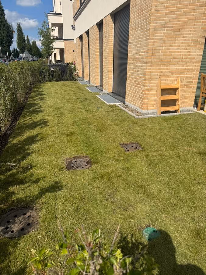 Rasenfläche am Klinkerbau mit bündig eingebauten Schachtdeckeln