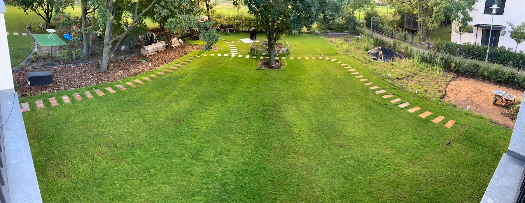 Große fertige Rasenfläche mit umlaufendem Trittplattenweg und altem Baumbestand