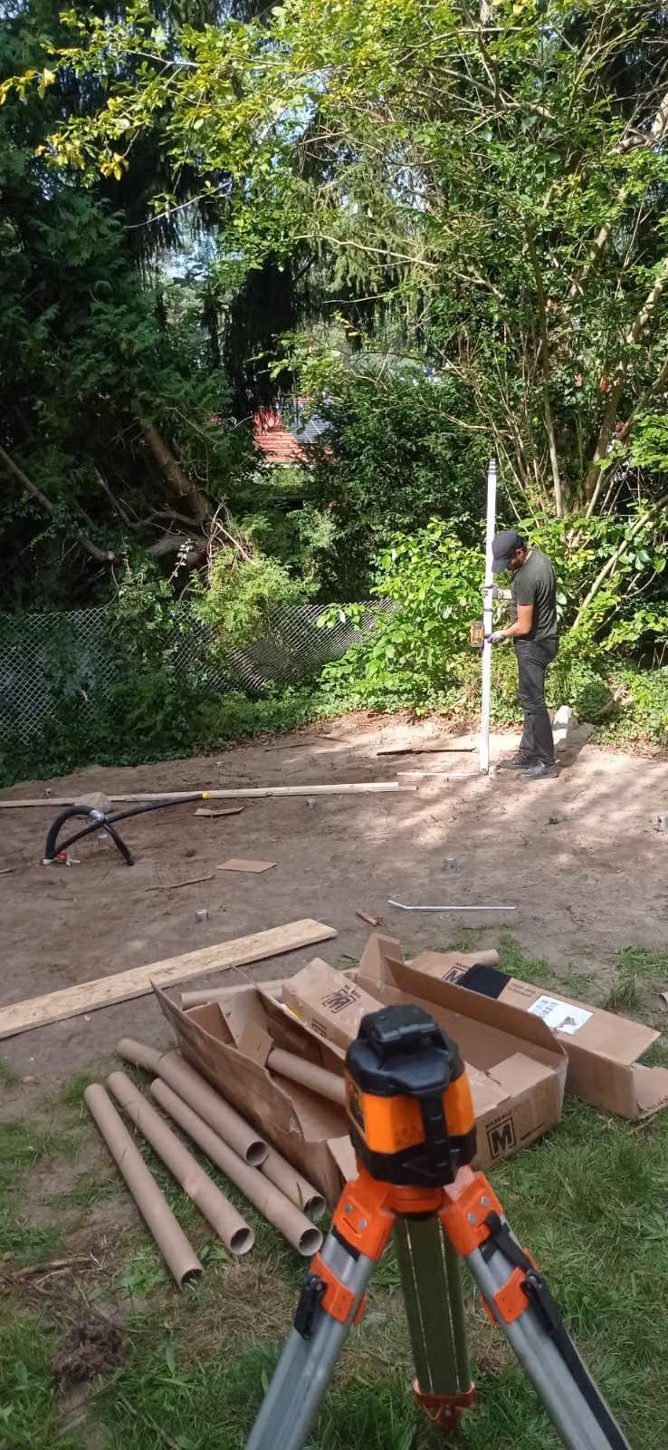 Rotationslaser auf dem Stativ im Vordergrund, dahinter arbeitet ein Mann mit der Nivellierlatte