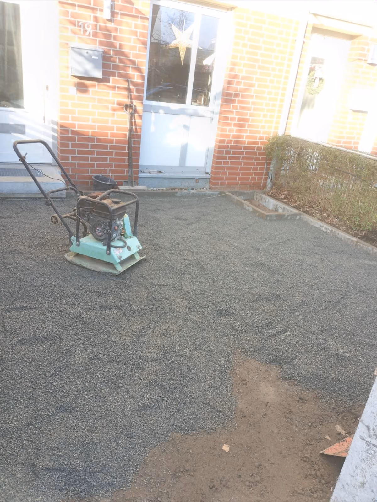 Rüttelplatte steht auf dem Splittbett vor einem Hauseingang