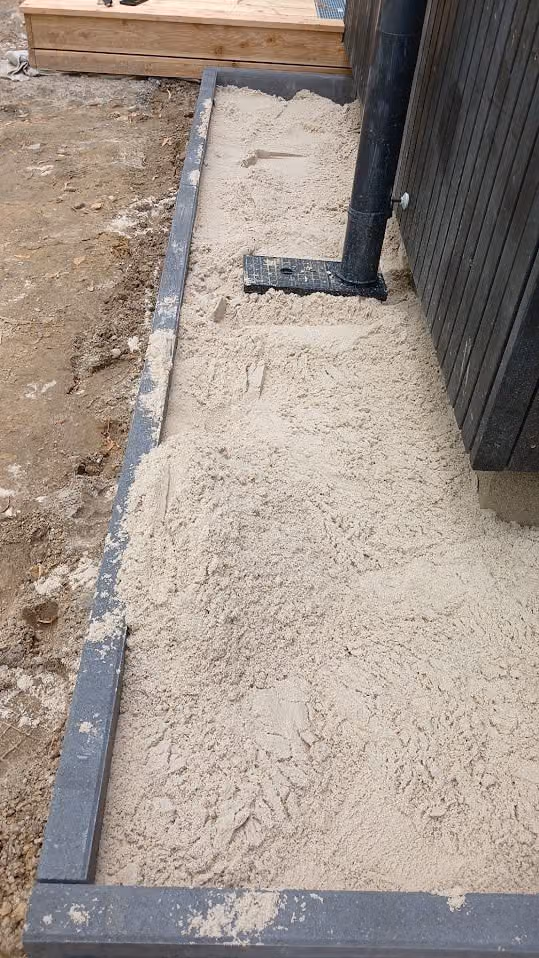 Abgezogenes Sandplanum zwischen gesetzten Metall-Randprofilen an der Fassade