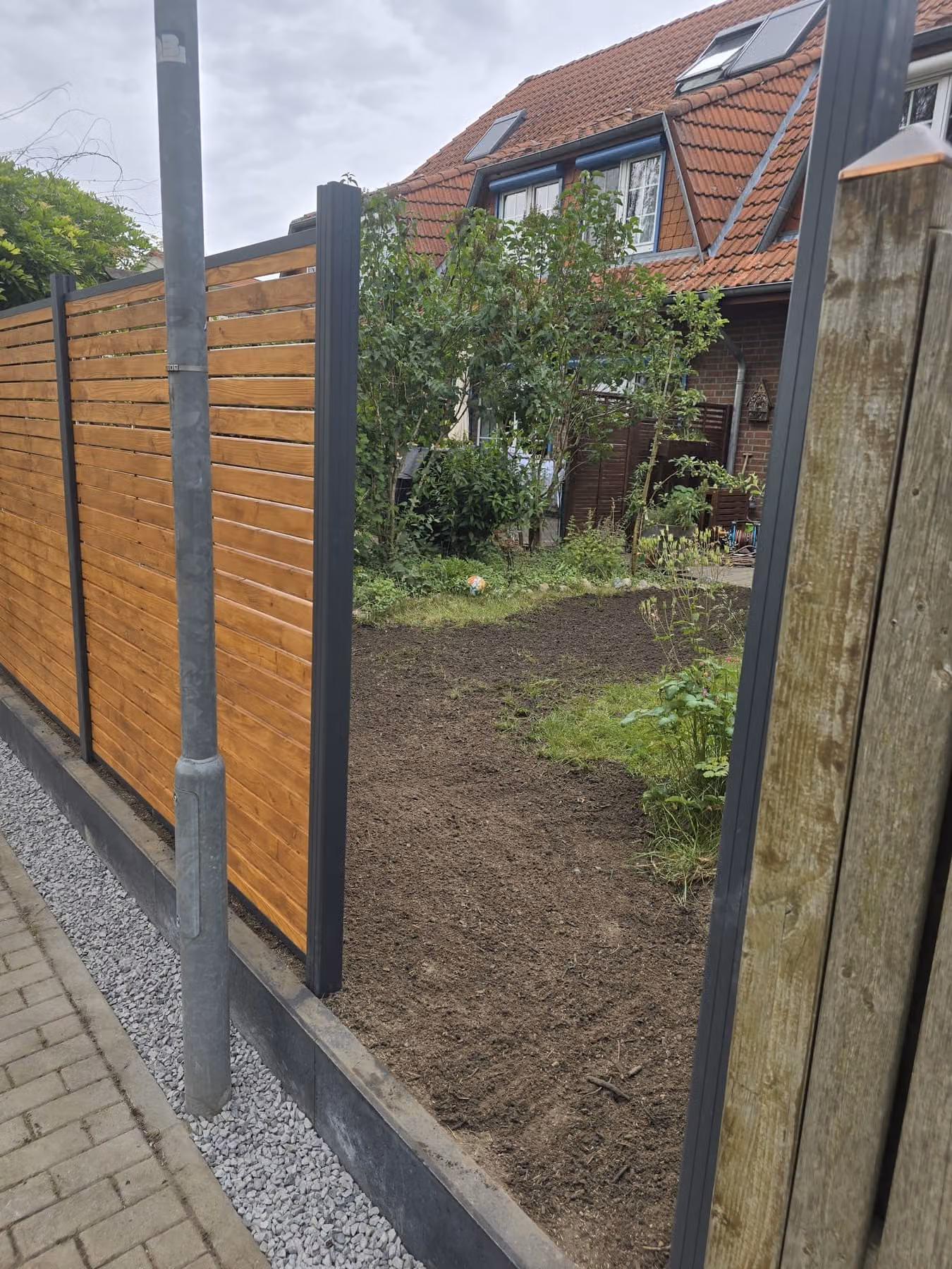 Sichtschutzzaun aus Holzlatten von der Gartenseite, dahinter die vorbereitete Vorgartenfläche