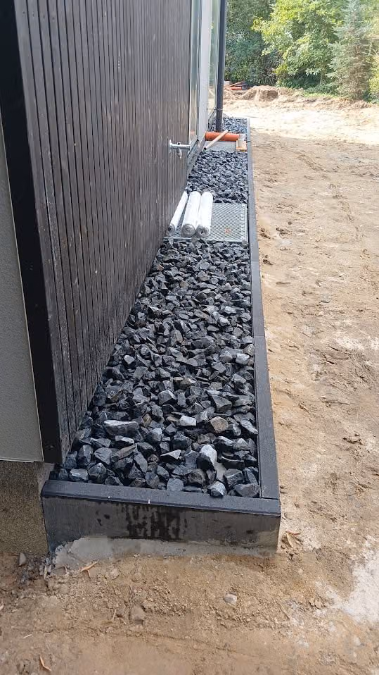 Spritzschutzstreifen aus Basaltsplitt mit Metallkante entlang der Hausfassade