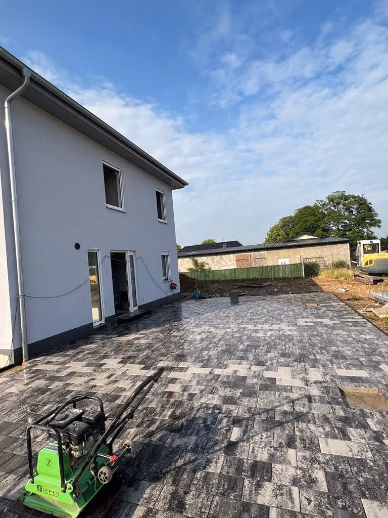 Große Terrassenfläche aus grau-weiß gemischtem Betonpflaster an einem Neubau