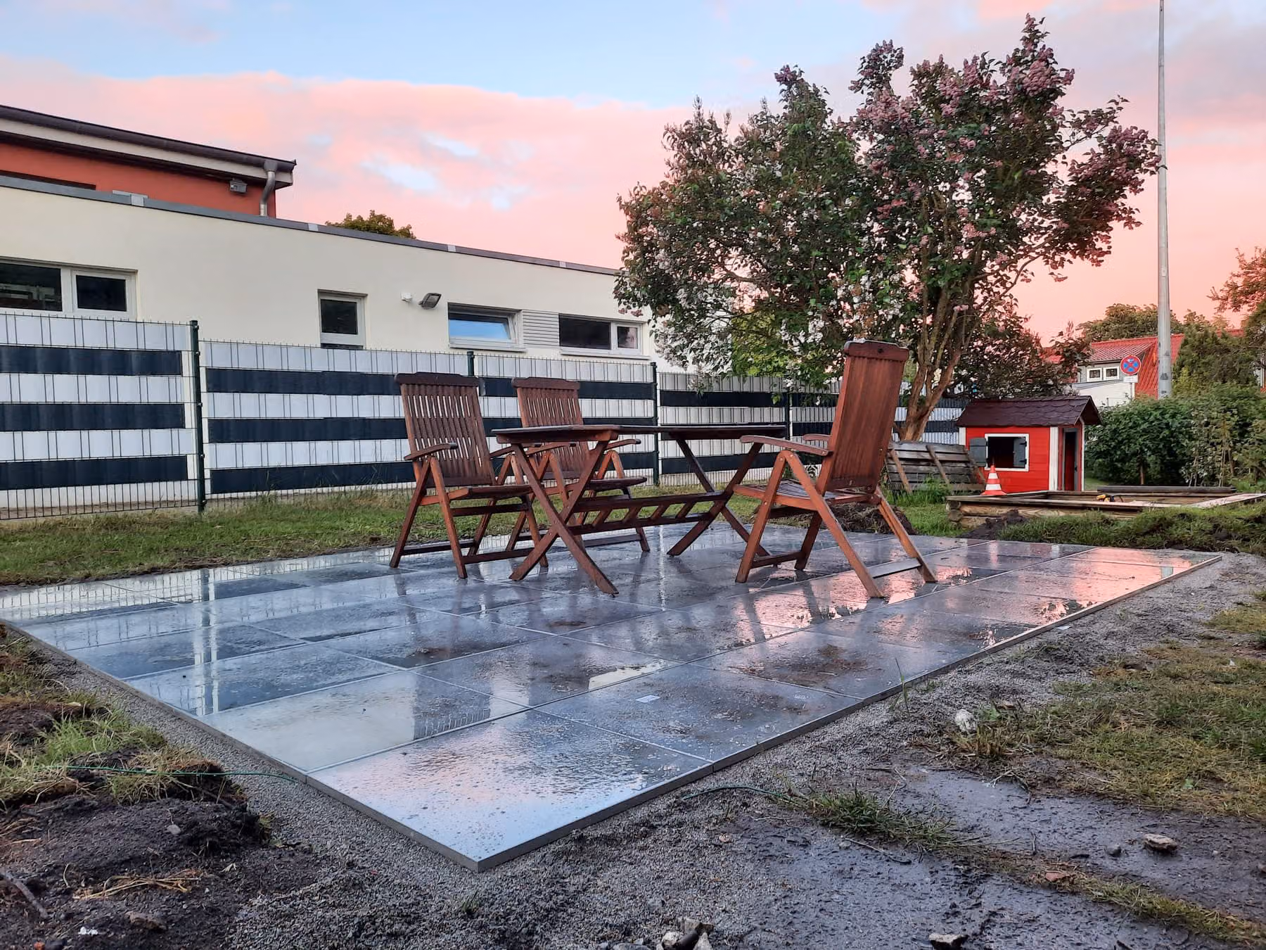 Fertige Terrasse aus großformatigen Platten mit Gartenmöbeln, nach dem Regen im Abendlicht