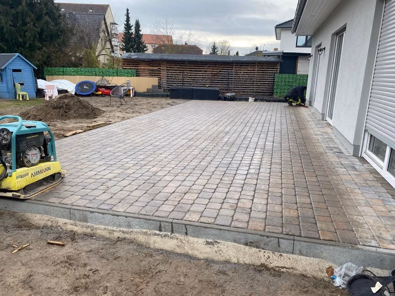 Fertig verlegte Pflasterfläche im Reihenverband am Haus, Rüttelplatte am Rand abgestellt