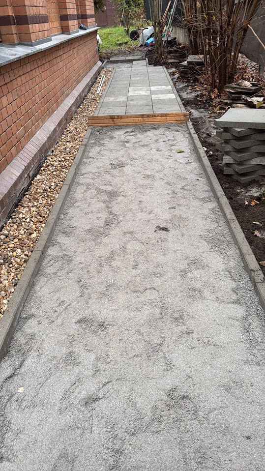 Abgezogenes Splittbett zwischen gesetzten Betonkanten, Platten liegen zum Verlegen bereit