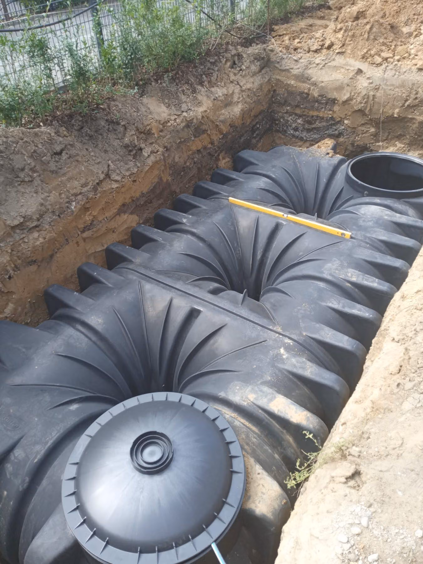 Großer Flachtank einer Zisterne in der Baugrube, Lage wird mit der Wasserwaage geprüft